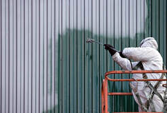 Peintre professionnel, à Victoriaville, portant un équipement de protection complet sur une nacelle. Il peinture le revêtement en métal d'un bâtiment.